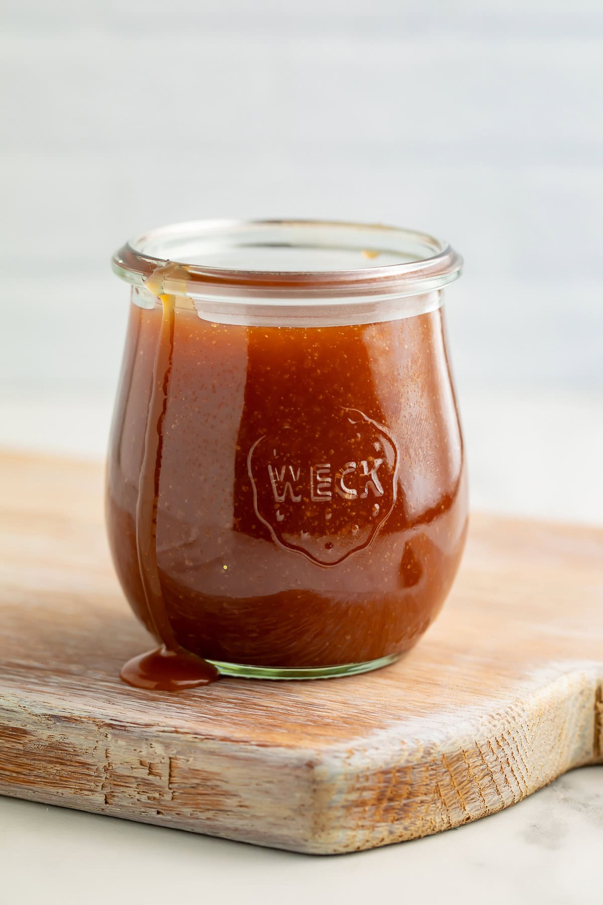 A jar of caramel sauce, sitting atop a wooden cutting board.