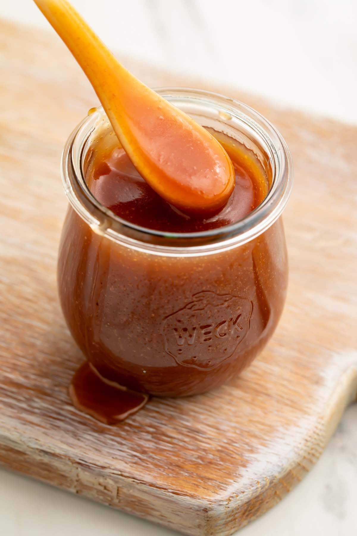 A spoonful of caramel sauce being lifted out of a glass jar of caramel sauce.