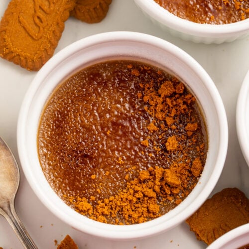 Biscoff cookie butter creme brulee in a round white ramekin on a table with broken cookie pieces.