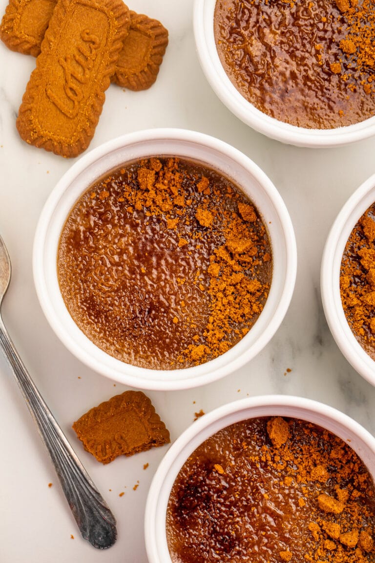 4 ramekins of cookie butter creme brulee on a table surrounded by Biscoff cookies.