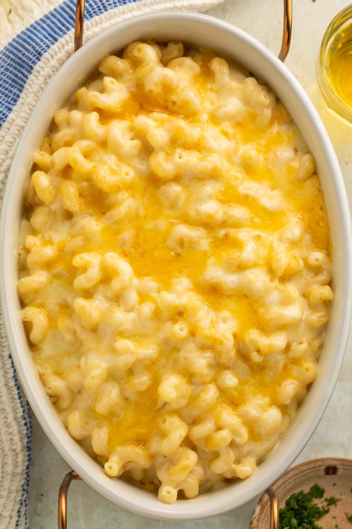 Overhead view of a large oval casserole dish holding a rich, creamy truffle mac and cheese on a table with a glass of white wine and a blue striped napkin.