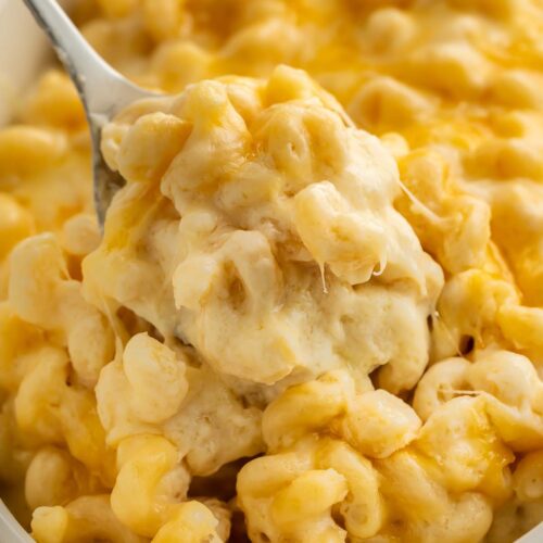 A scoop of truffle mac and cheese being held up over a casserole dish by a large silver spoon.