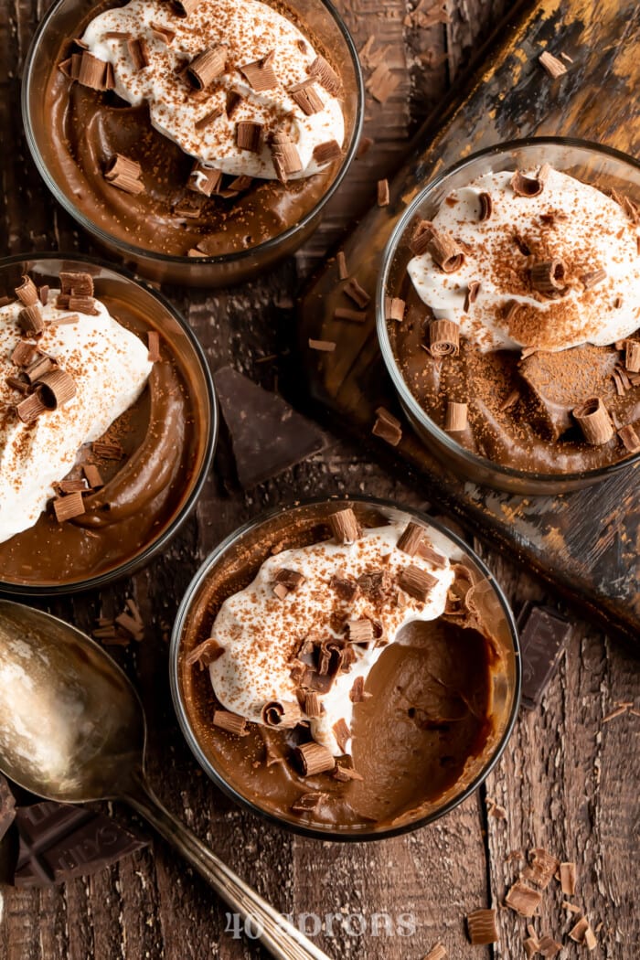 Overhead view of 4 glass cups holding avocado chocolate mousse topped with coconut cream. One bite is missing from one of the jars.