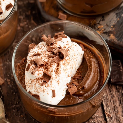 Overhead angled view of 4 jars of avocado chocolate mousse topped with whipped coconut cream.