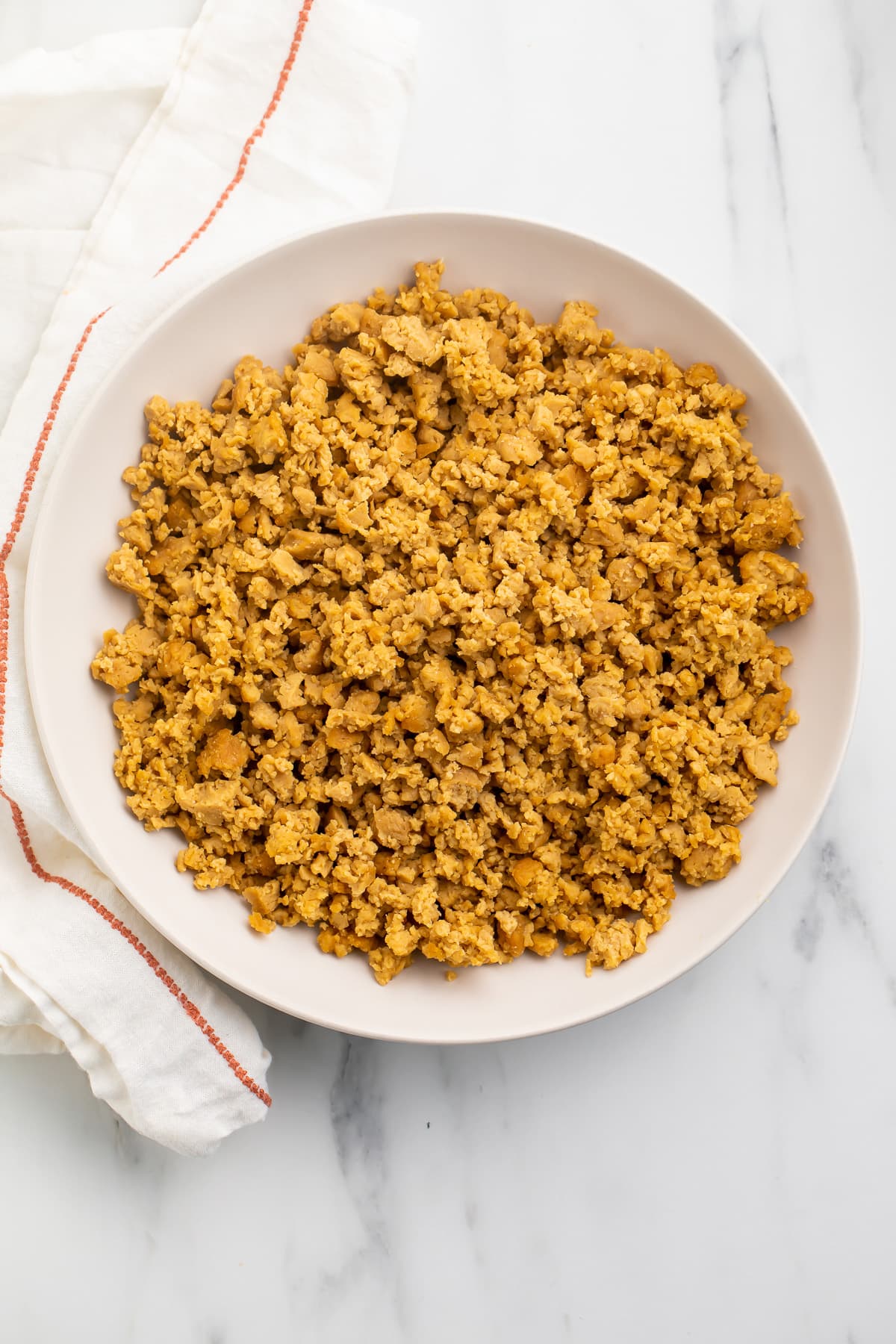 Overhead view of a bowl of seitan ground "beef" crumbles on a marble countertop.