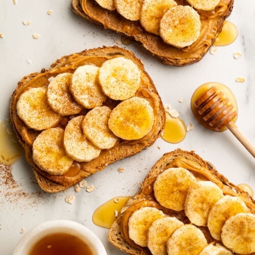 Overhead view of 3 slices of peanut butter banana toast drizzled with honey then topped with a dash of cinnamon and sea salt.