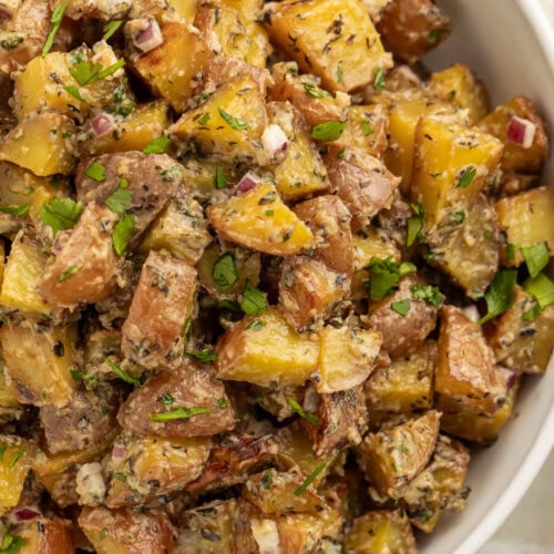 Overhead view of a large bowl of roasted potato salad with diced roasted potatoes, fresh herbs, and red onions.