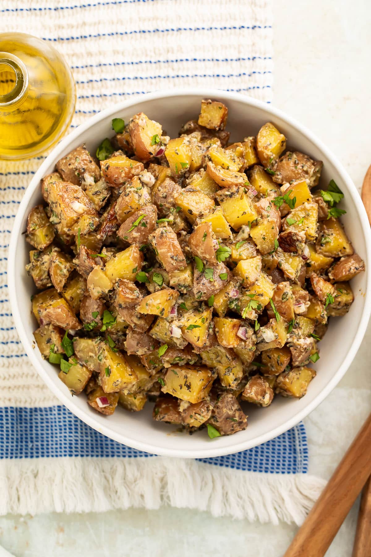 Overhead view of a large bowl of roasted potato salad with diced roasted potatoes, fresh herbs, and red onions.