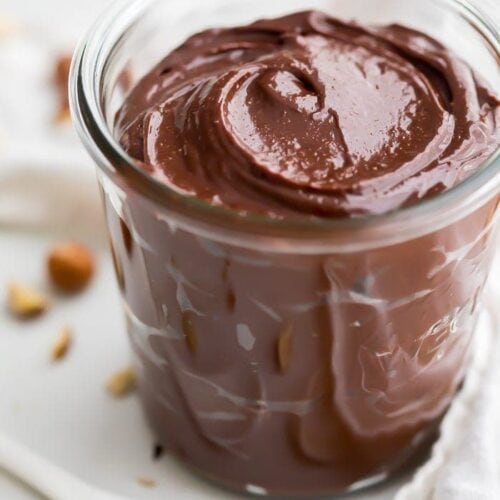 A jar of vegan Nutella with hazelnuts in the background