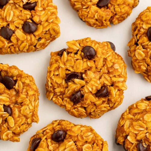 No-bake pumpkin oatmeal cookies dotted with chocolate chips arranged on a sheet of parchment paper.