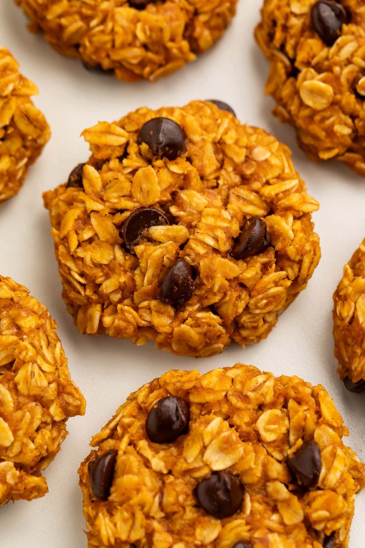 No-bake pumpkin oatmeal cookies dotted with chocolate chips arranged on a sheet of parchment paper.