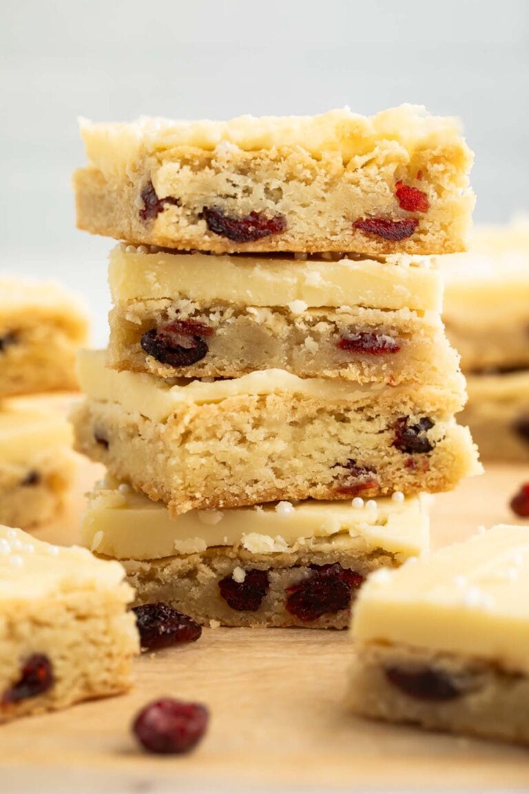 A stack of four square cranberry white chocolate cookie bars on a sheet of parchment paper.