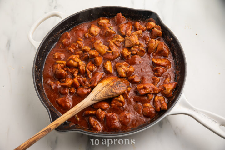 Chicken thighs with spiced butter, tomato sauce, and a wooden spoon in a large wok.