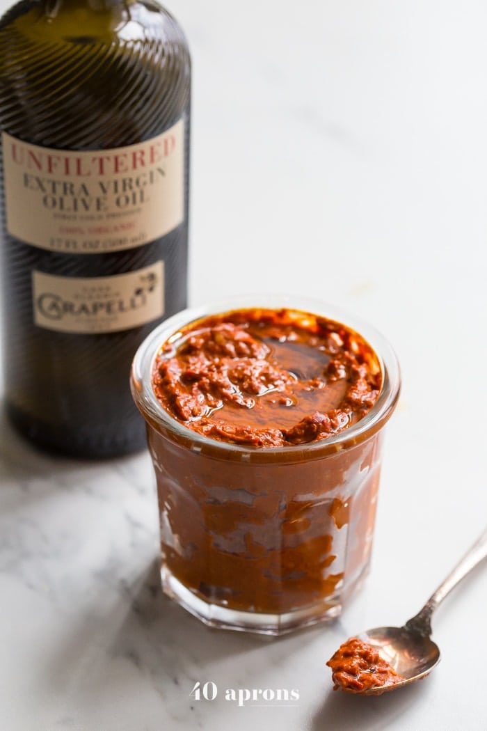 homemade harissa in a small glass dish with a bottle of carapelli olive oil in the background