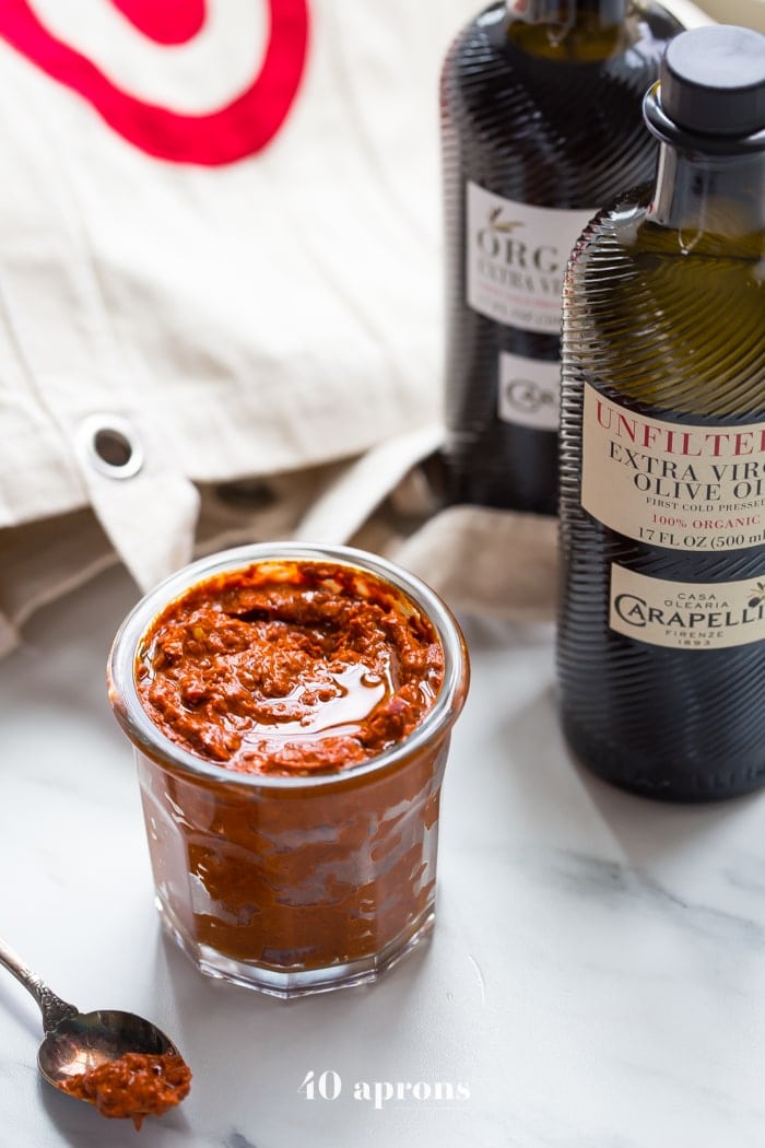 a small glass dish with homemade harissa spice paste next to a bottle of olive oil