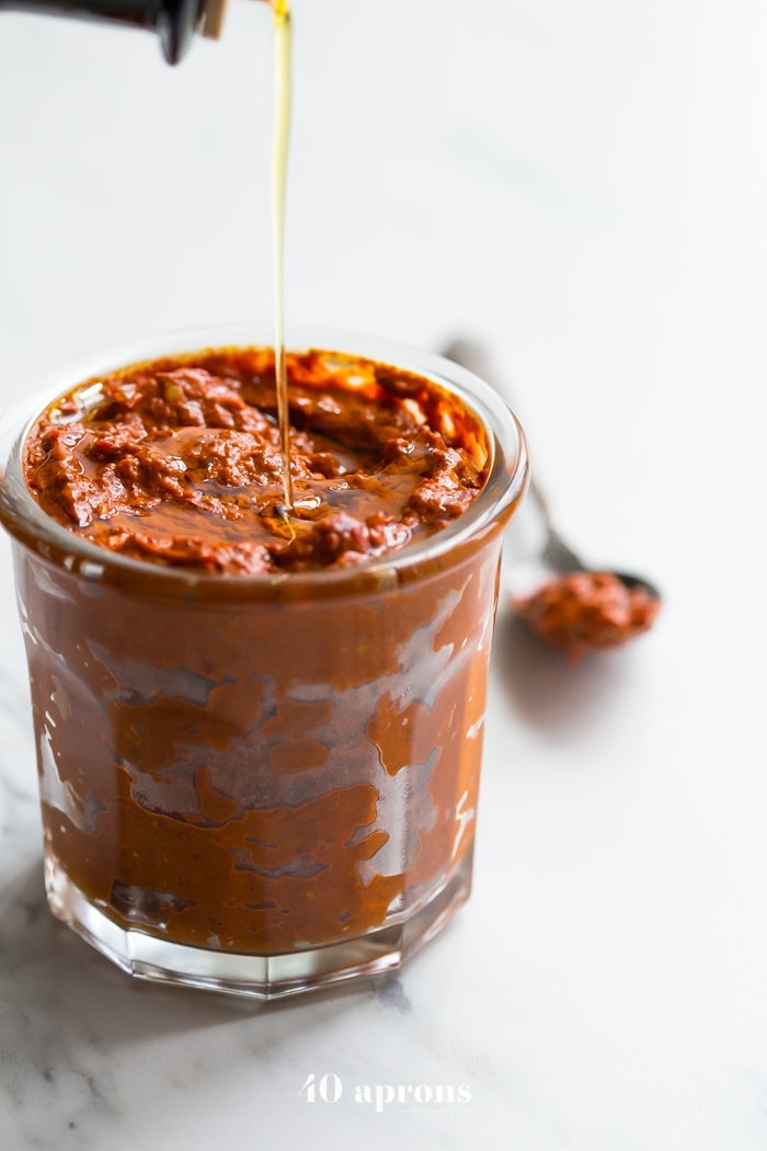 olive oil being drizzled on top of a small glass jar of homemade harissa spice paste