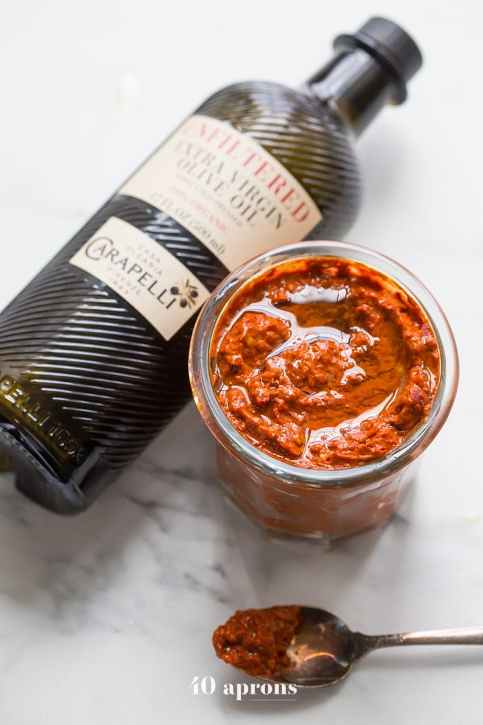 overhead shot of a small jar of homemade Harissa next to a bottle of virgin olive oil 