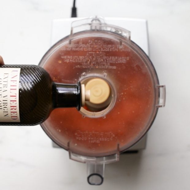 olive oil being drizzled into a food processor with homemade harissa