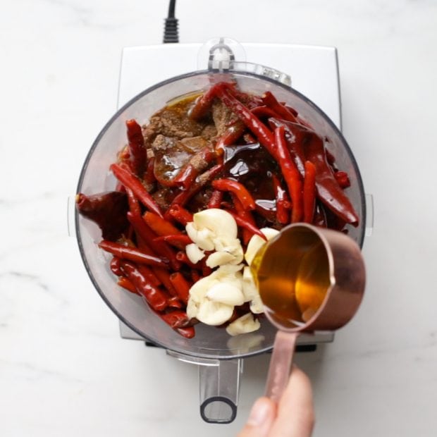 olive oil being added to fresh and dried chilies and garlic in a food processor bowl