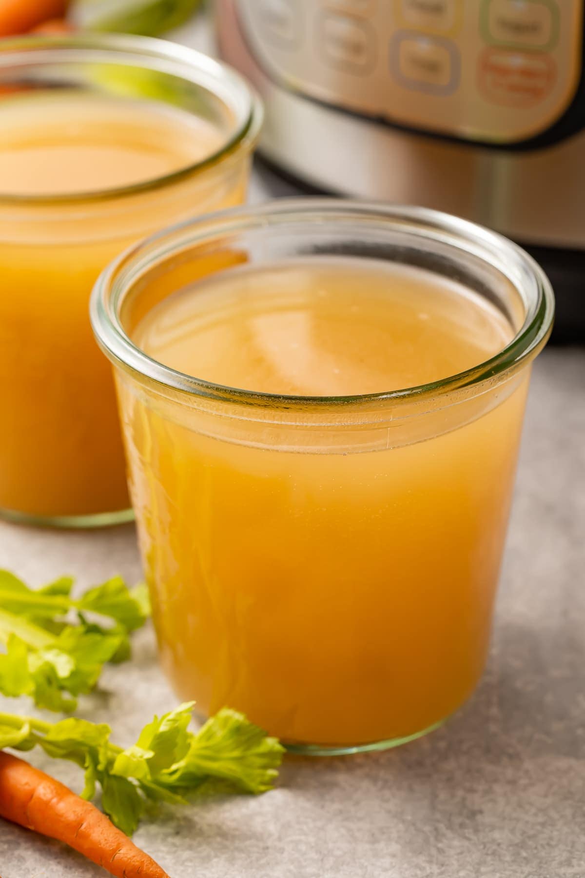 instant Pot bone broth in glasses next to an Instant Pot pressure cooker