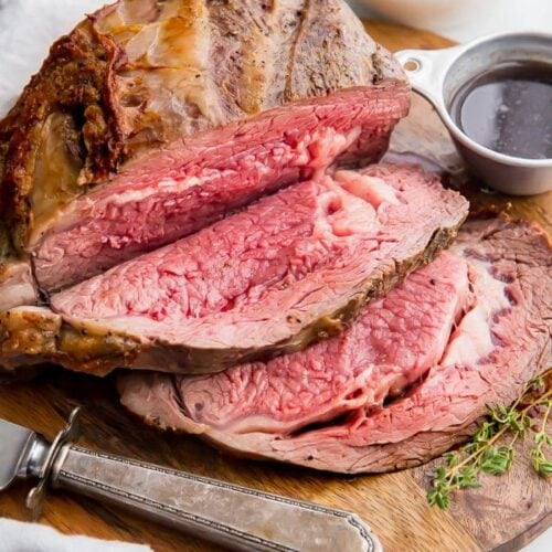 Medium rare prime rib sliced on a board with au jus in a cup