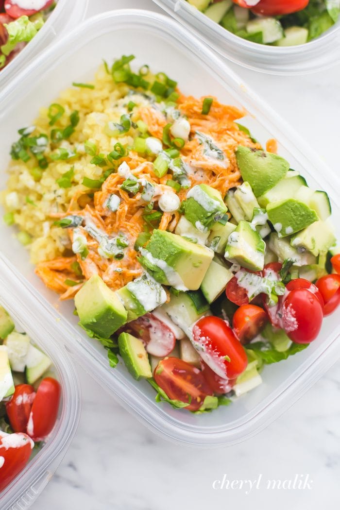 Buffalo chicken meal prep with avocado, cauliflower rice, and ranch dressing in container