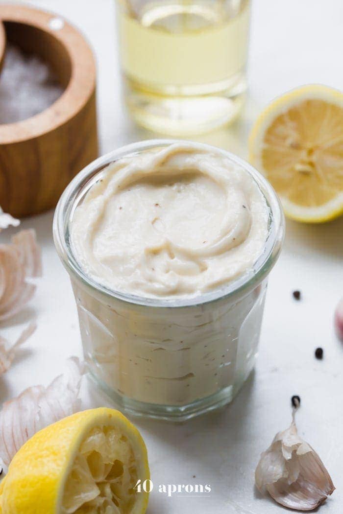 Whole30 Caesar dressing in a jar with lemons, garlic, peppercorns, and light tasting olive oil in a bottle