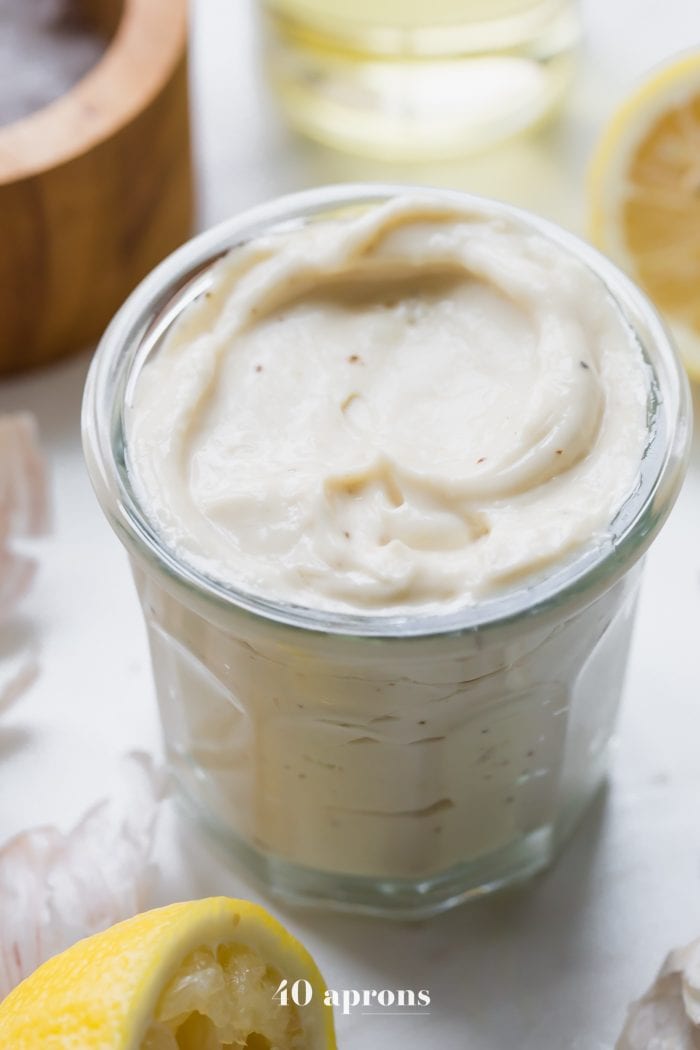 Whole30 Caesar dressing in a jar with lemons, garlic, peppercorns, and light tasting olive oil in a bottle