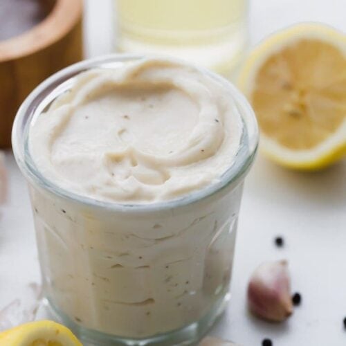 Whole30 Caesar dressing in a jar with lemons, garlic, peppercorns, and light tasting olive oil in a bottle