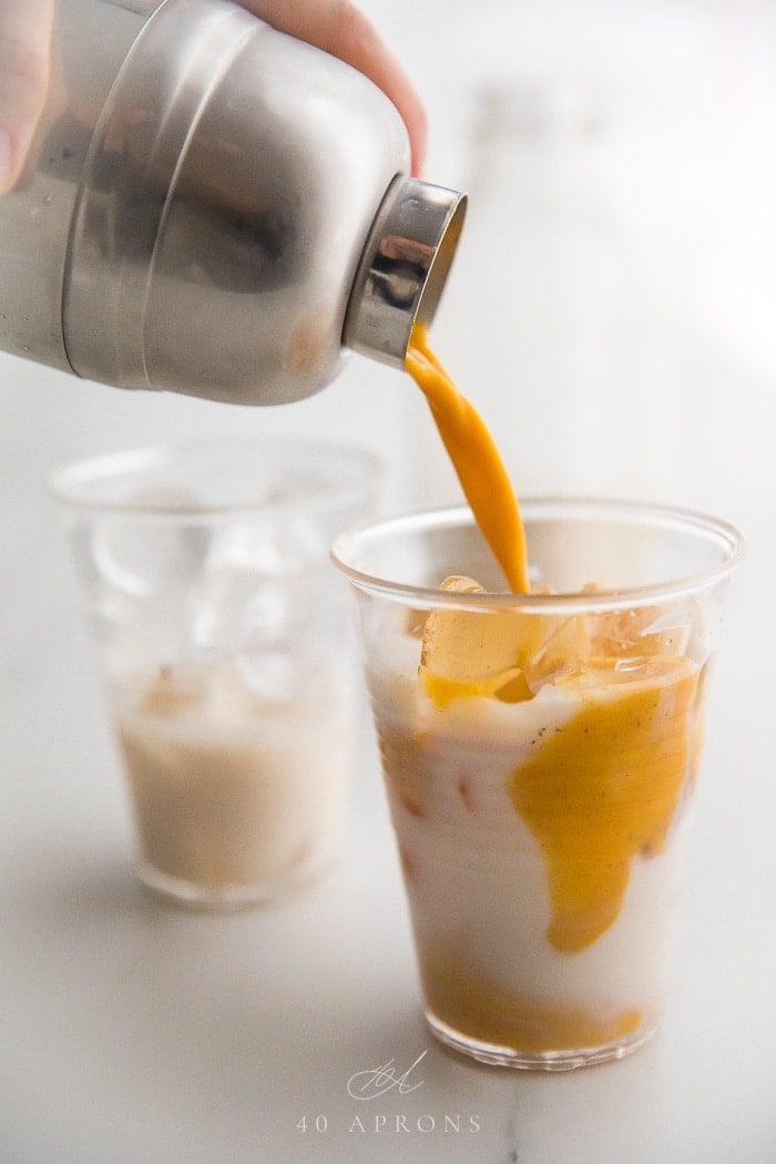 Golden milk mixture pouring over milk and ice in a cup