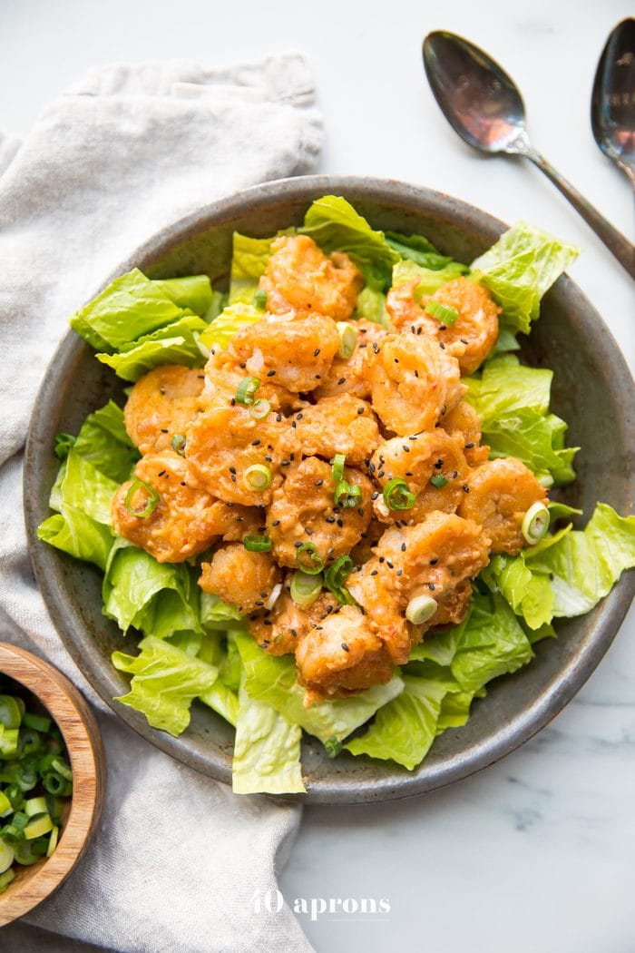 Whole30 bang bang shrimp topped with green onions and sesame seeds on a bed of romaine lettuce