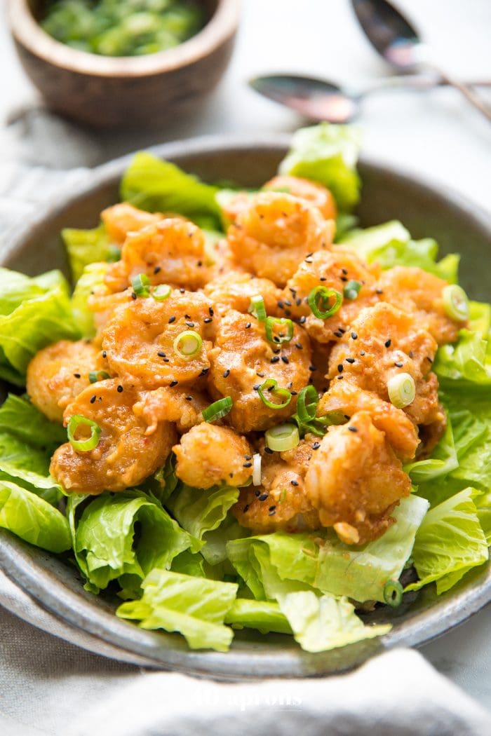 Whole30 bang bang shrimp topped with green onions and sesame seeds on a bed of romaine lettuce