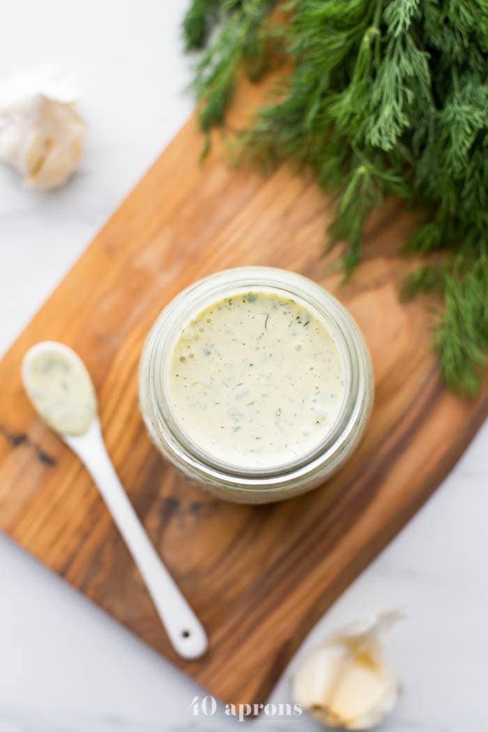 Whole30 ranch dressing in a jar on a board with fresh herbs in background