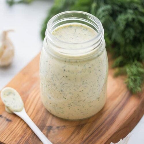 Whole30 ranch dressing in a jar on a board with fresh herbs in background