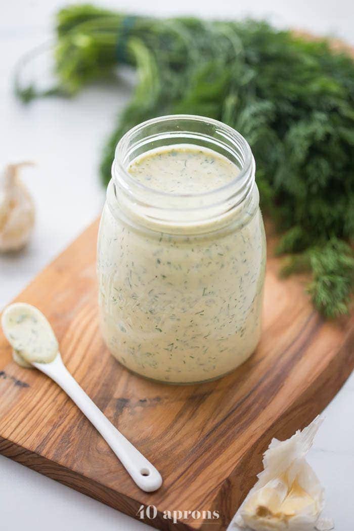 Whole30 ranch dressing in a jar on a board with fresh herbs in background