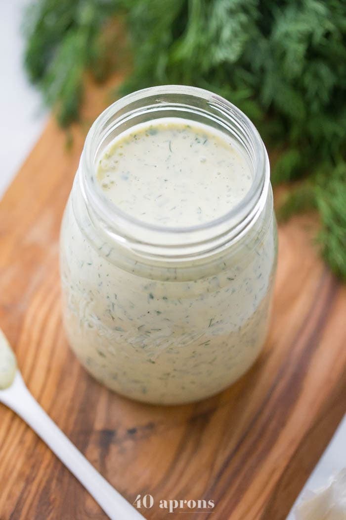 Whole30 ranch dressing in a jar on a board with fresh herbs in background