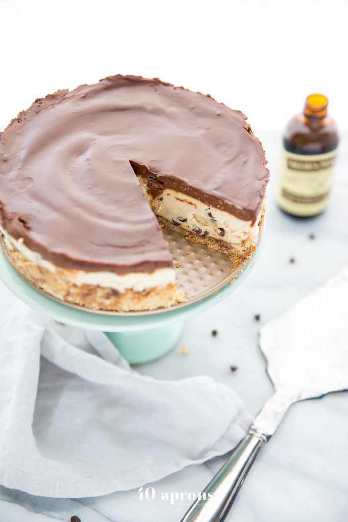 Whole vegan no bake cookie dough cheesecake on a cake stand with a slice cut out