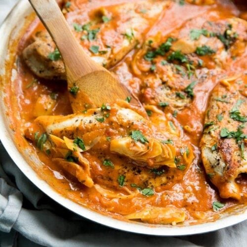 Creamy tomato artichoke chicken (Whole30, paleo) in a skillet with a spoon lifting up one chicken piece