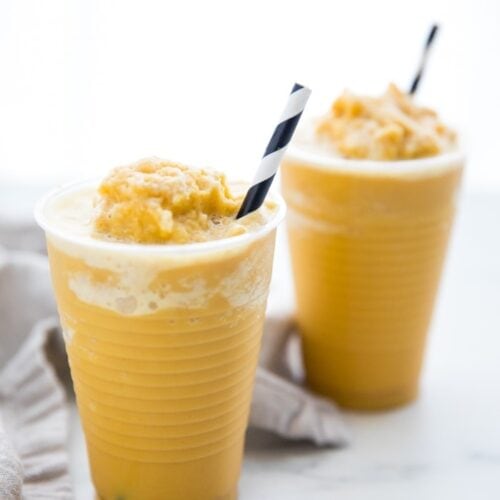 Two frozen golden milk turmeric frappuccinos in to-go cups with black and white straws