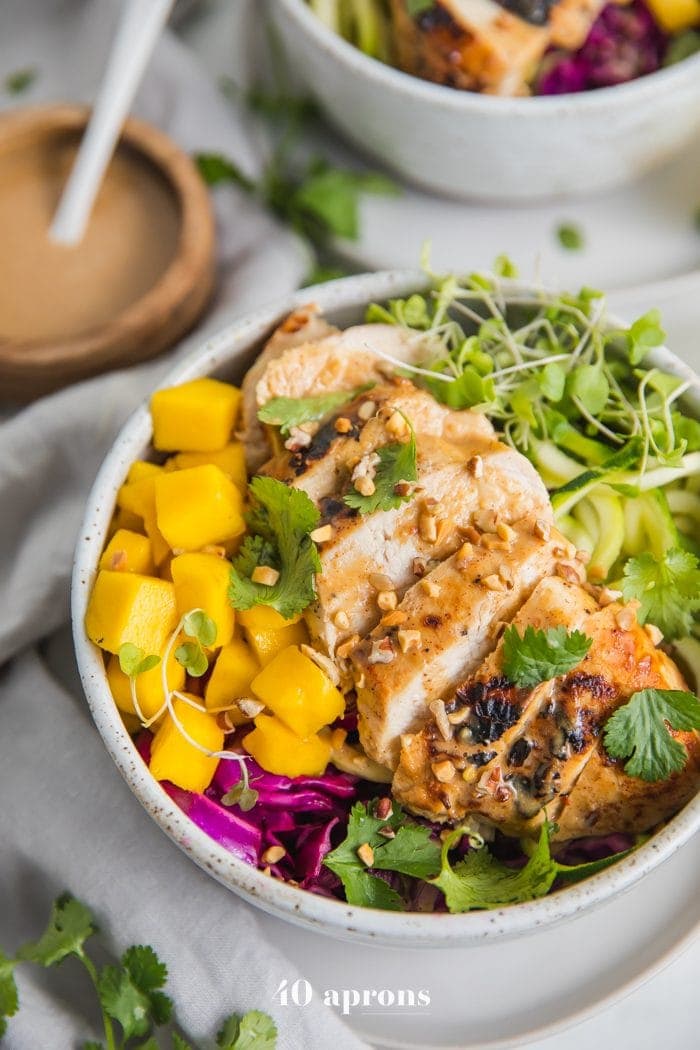 Whole30 Thai chicken zoodle bowls with "peanut sauce" in a bowl with garnishes