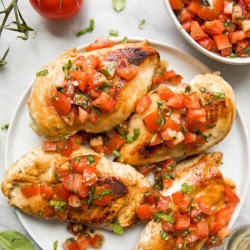 Bruschetta chicken on a plate with fresh basil, bruschetta, and more bruschetta chicken in background