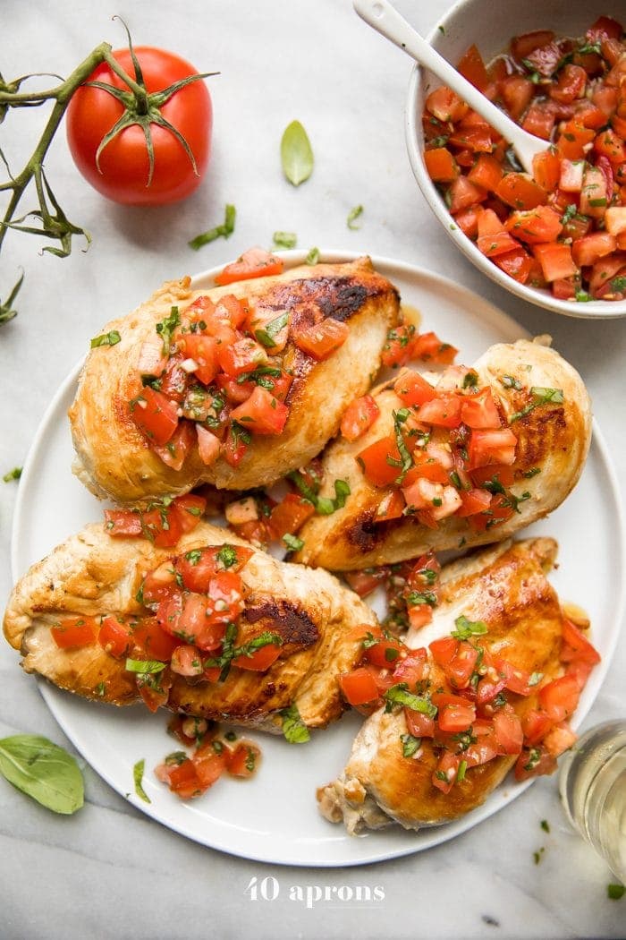 Bruschetta chicken on a plate with fresh basil, bruschetta, and more bruschetta chicken in background