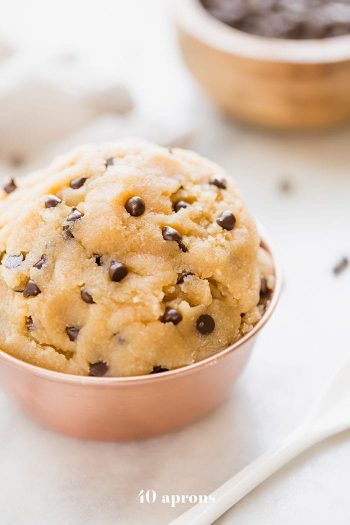 Vegan healthy cookie dough in a copper bowl with a bowl of chocolate chips in the corner