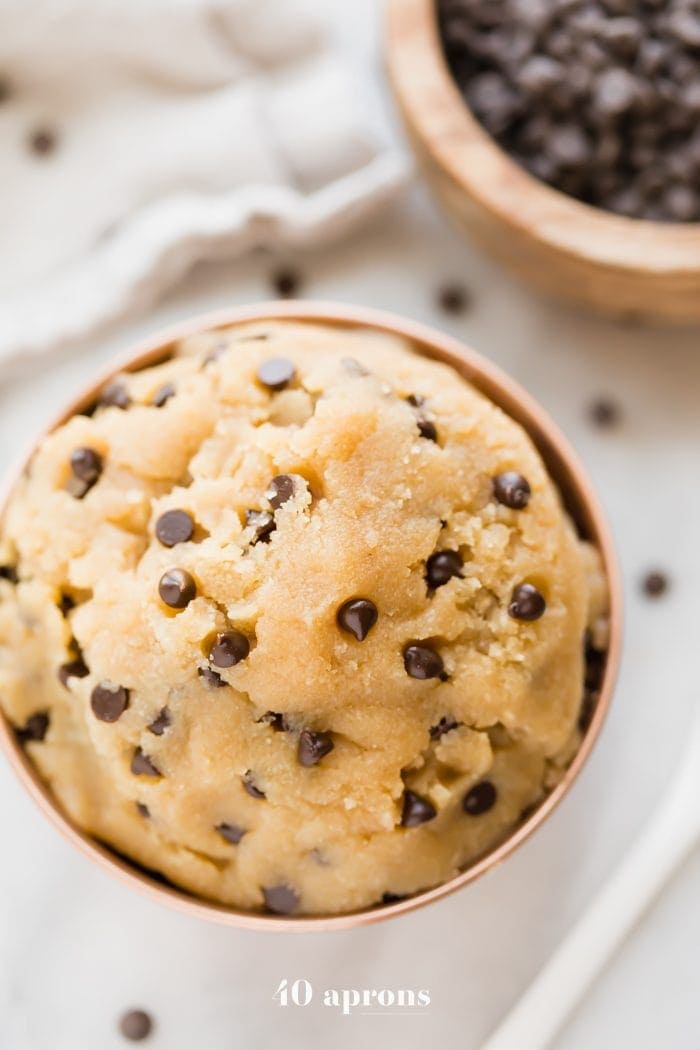 Vegan healthy cookie dough in a copper bowl with a bowl of chocolate chips in the corner