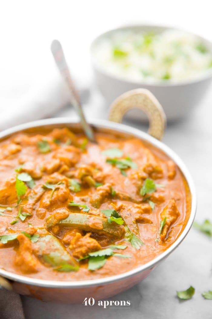 Instant Pot chicken tikka masala in a copper serving bowl with chopped cilantro and cauliflower rice in the background