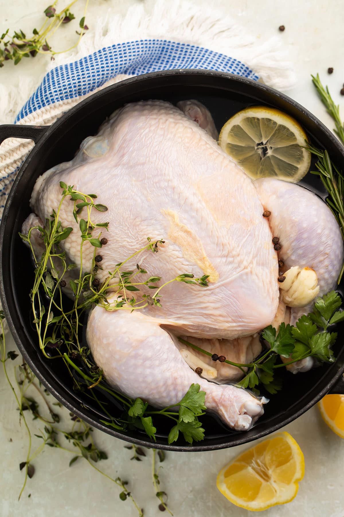 A whole, uncooked chicken in a large pot filled with a quick chicken brine of water, lemon, and herbs.