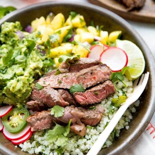 Whole30 steak taco bowl with steak, guacamole, pineapple salsa, pickled radish, and cauliflower rice