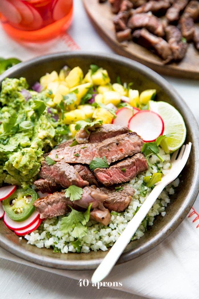 Whole30 steak taco bowls with steak, guacamole, pineapple salsa, pickled radish, and cauliflower rice