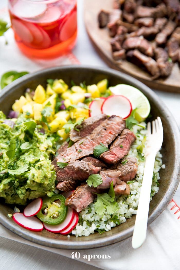 Whole30 steak taco bowls with steak, guacamole, pineapple salsa, pickled radish, and cauliflower rice