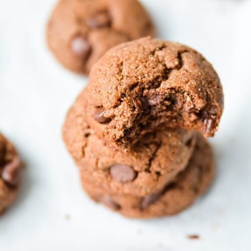 a stack of Paleo Double Chocolate Fudge Cookies on a lined baking tray with a bit taken from the top one.